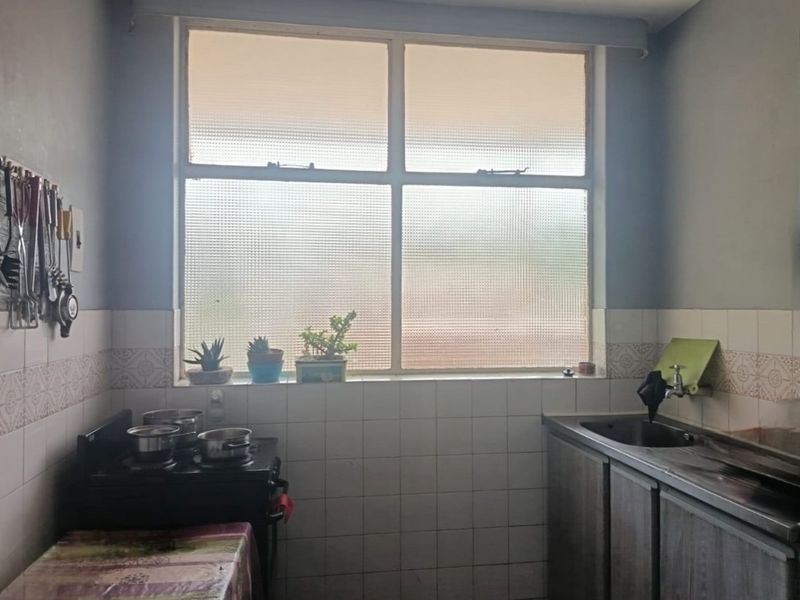 A functional kitchen area featuring a stainless steel sink, tiled splashback, and built-in cabinetry under a large textured glass window.