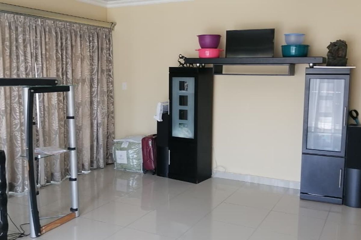 A spacious living room featuring large floor-to-ceiling curtains and neutral tiled flooring, providing a versatile area for relaxation and entertainment.