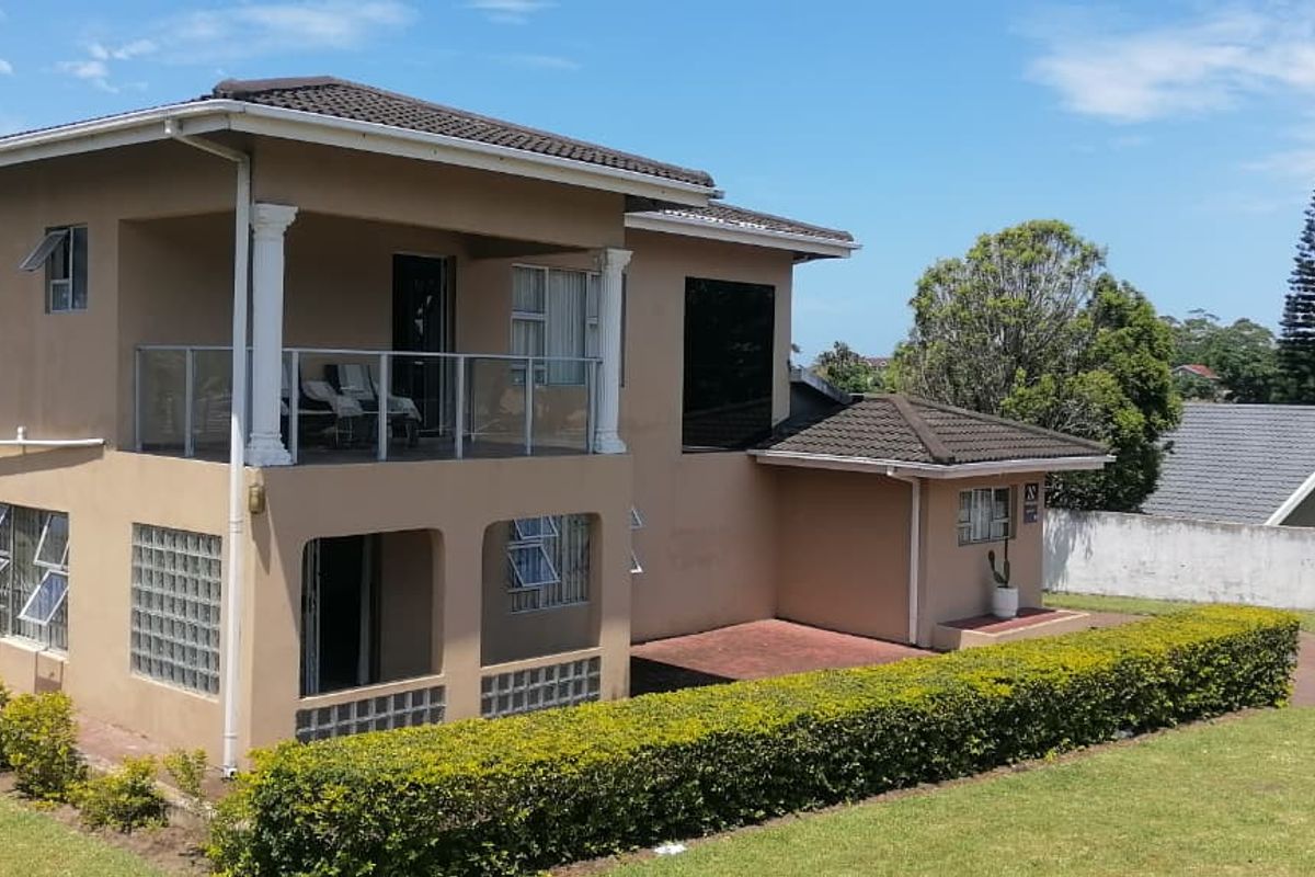A two-story residential property featuring a covered upper-level balcony with glass balustrades, glass block accents, and a surrounding landscaped garden.