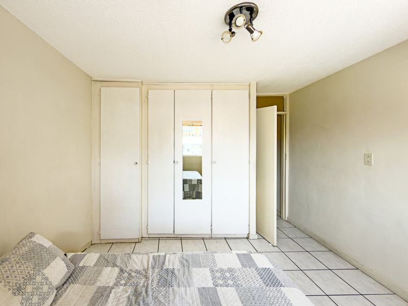 A bedroom featuring built-in cupboards with a central mirror panel, tiled flooring, and a standard ceiling light fixture.