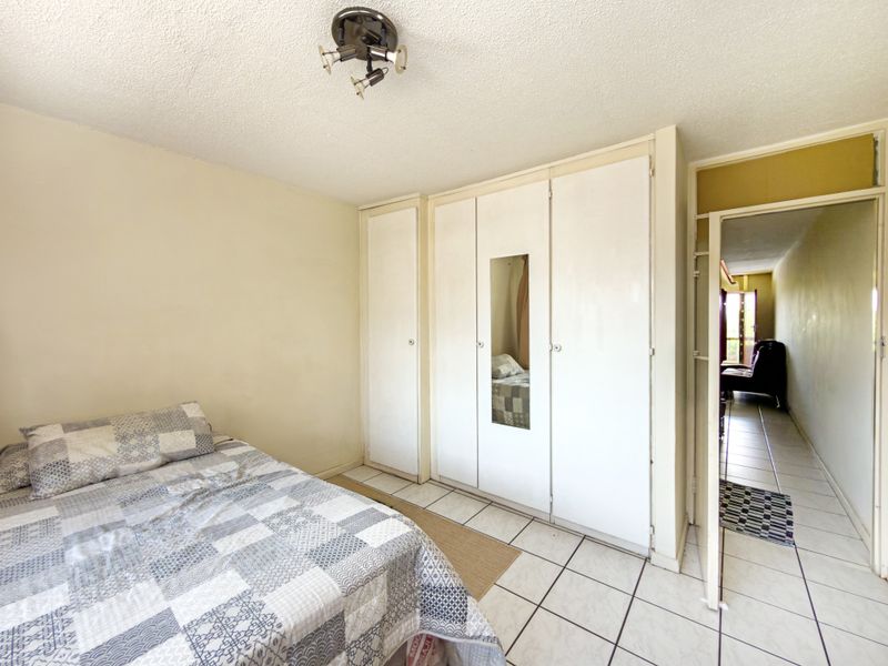 A bedroom featuring built-in wardrobes and tiled flooring, offering a functional space with potential for cosmetic updates.