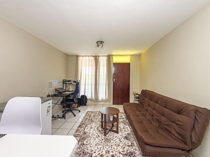 A functional living area featuring tiled flooring, a solid entrance door with a transom window, and neutral wall finishes.