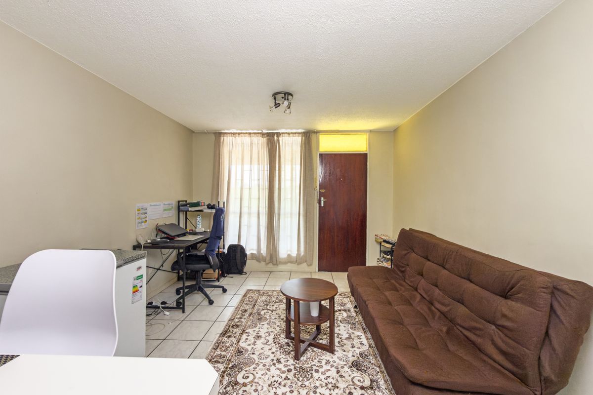 A functional living area featuring tiled flooring, a solid entrance door with a transom window, and neutral wall finishes.