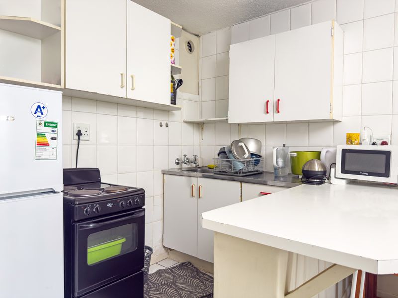 A compact kitchen featuring white cabinetry, a tiled backsplash, and a freestanding electric stove, offering a functional layout with potential for modernization.