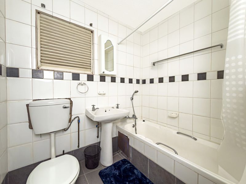A dated bathroom featuring a pedestal basin, bathtub with shower mixer, and toilet, finished with white and black tiled walls and grey floor tiles.