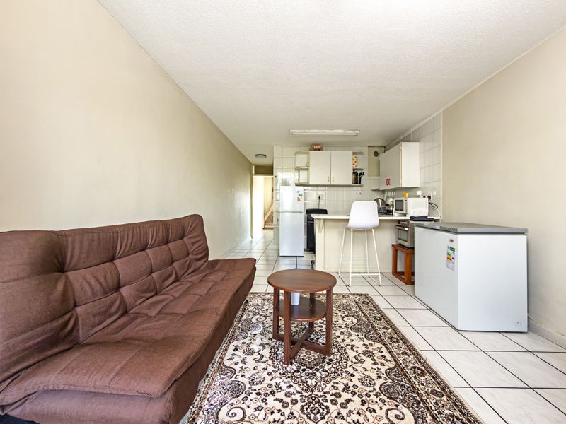 Open-plan living area featuring a compact kitchen with tiled backsplash and breakfast counter, finished with neutral wall tones and tiled flooring throughout.