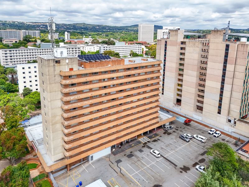 Aerial view of a high-rise apartment building featuring a rooftop solar array, telecommunications mast, and an adjacent paved parking area.