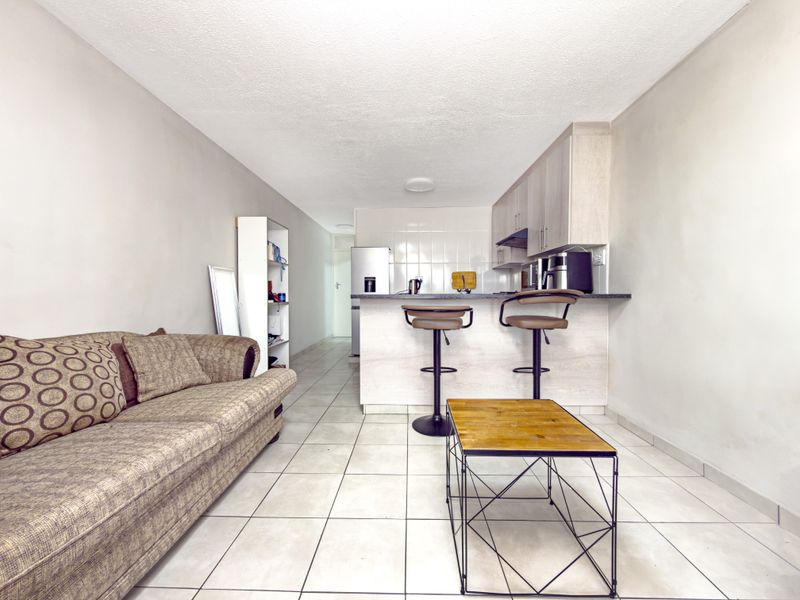 Open-plan living area featuring a functional kitchen with built-in cabinetry, breakfast bar, and tiled flooring throughout.