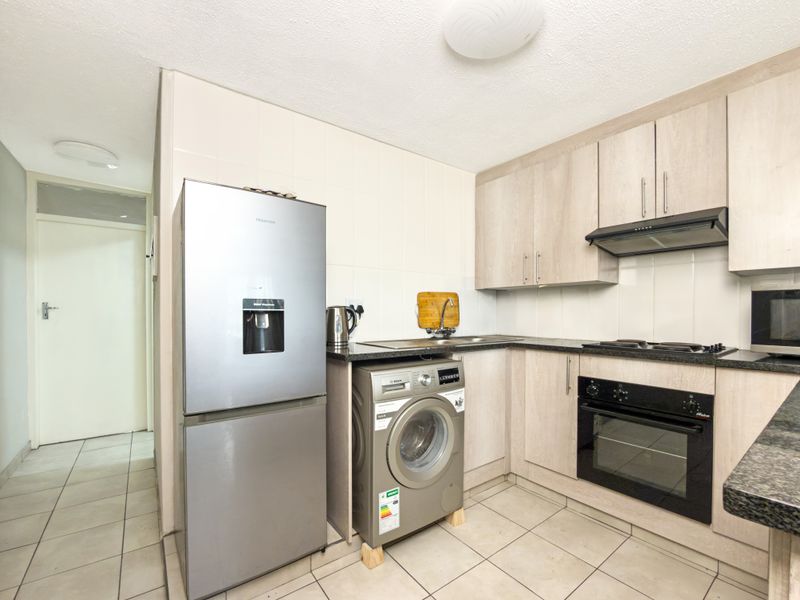 Compact kitchen featuring light wood-finish cabinetry, granite countertops, built-in oven, hob, extractor fan, and tiled flooring with a neutral backsplash.