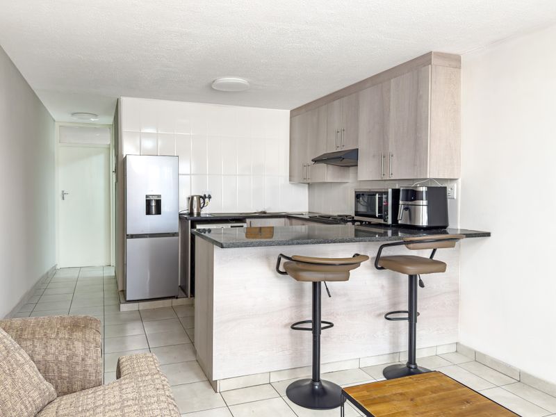 Open-plan kitchen featuring granite countertops, light wood-finish cabinetry, and ceramic wall tiling, seamlessly integrated with the living area.