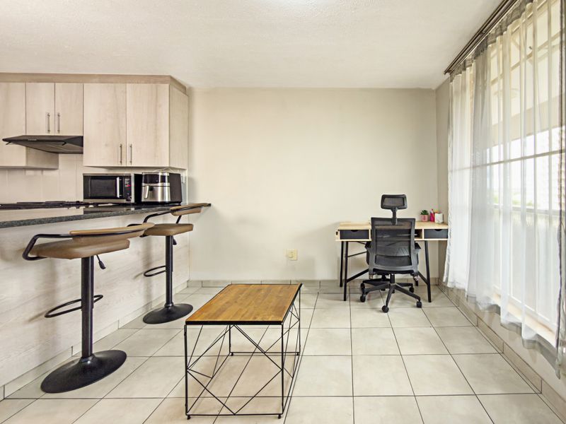 Open-plan living area featuring a kitchen with built-in cabinetry, granite countertops, and tiled flooring, adjacent to a bright space with large windows.