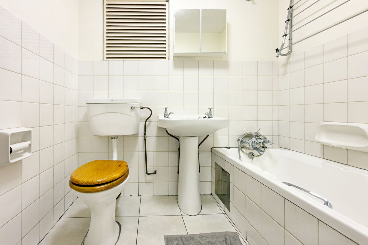 A dated bathroom featuring a pedestal basin, toilet, and bathtub with wall-to-wall tiling and a wall-mounted medicine cabinet.