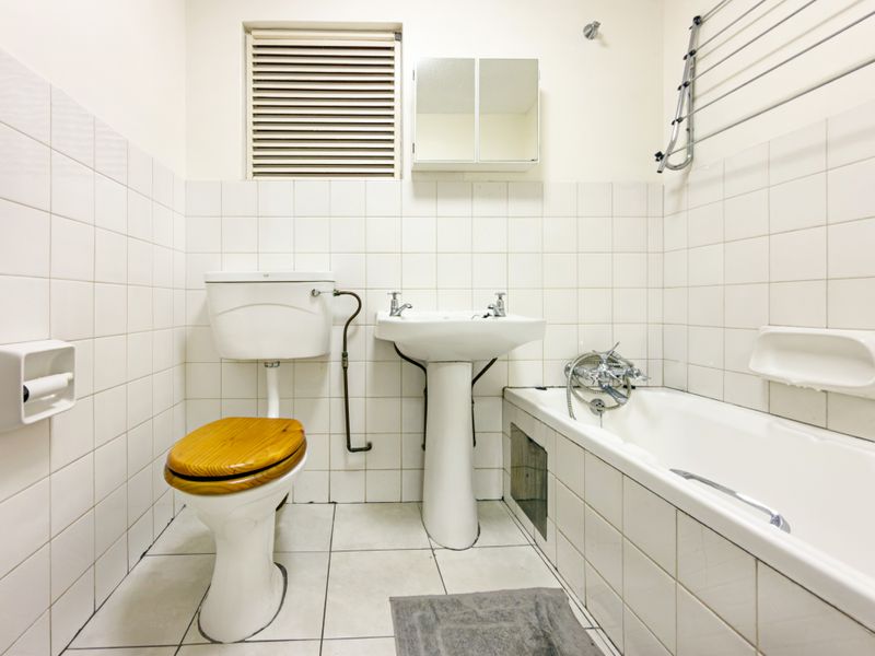 A dated bathroom featuring a pedestal basin, toilet, and bathtub with wall-to-wall tiling and a wall-mounted medicine cabinet.