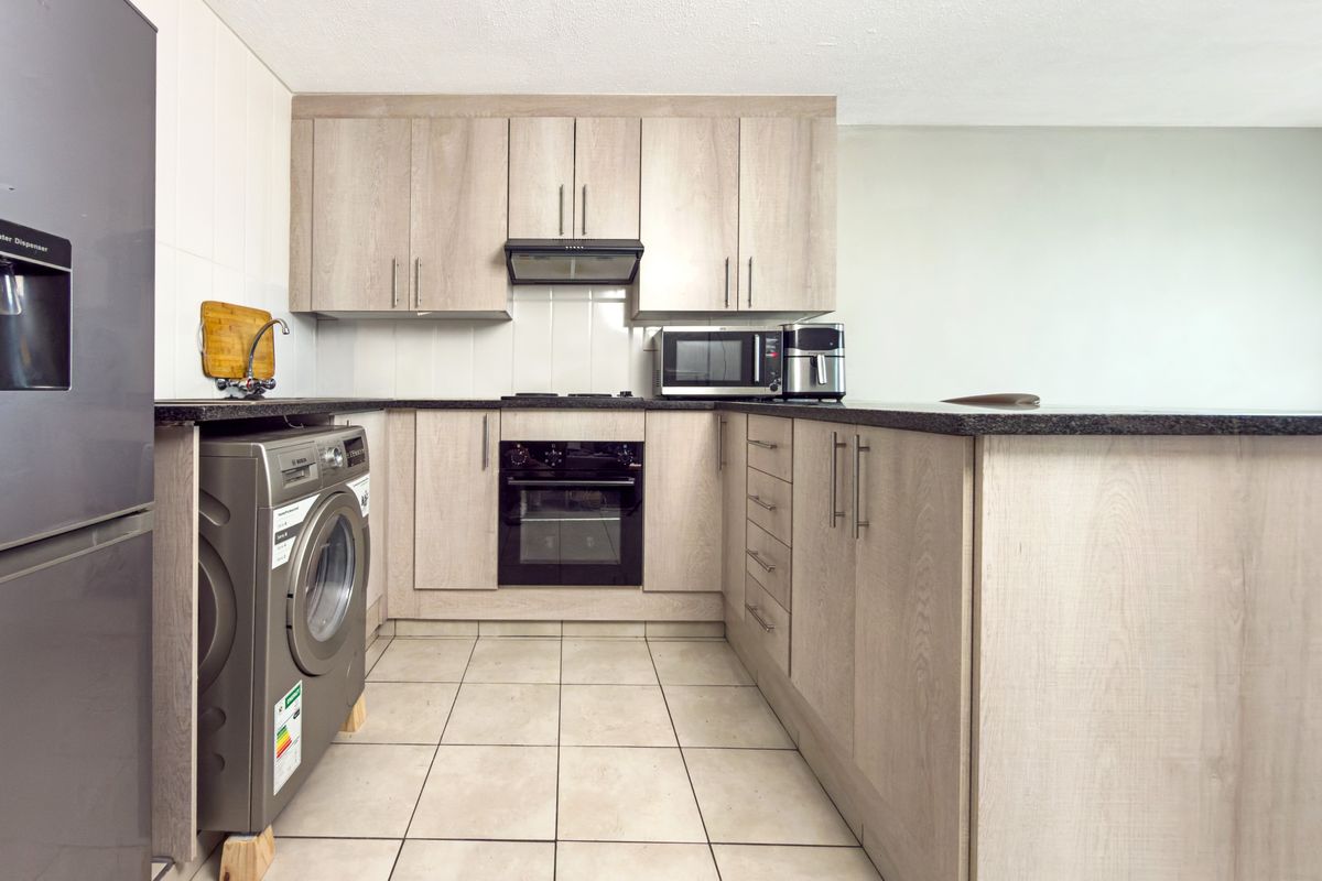 Modern kitchen featuring light wood-finish cabinetry, granite countertops, built-in oven, extractor fan, and tiled flooring in a functional layout.
