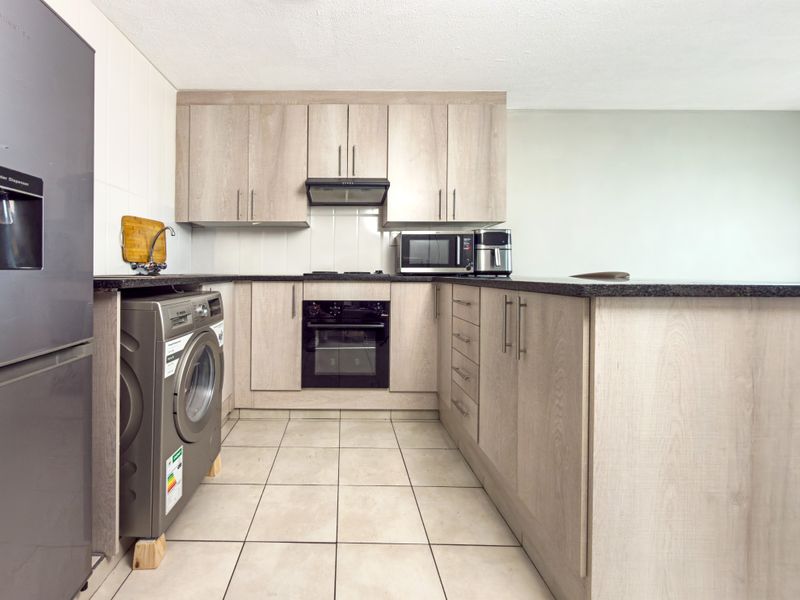 Modern kitchen featuring light wood-finish cabinetry, granite countertops, built-in oven, extractor fan, and tiled flooring in a functional layout.