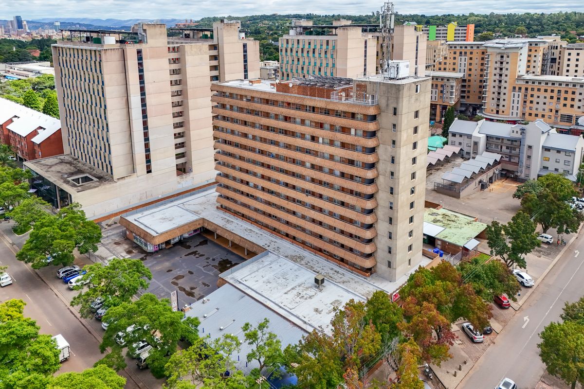 Aerial view of a multi-story apartment building featuring a flat roof, exterior facade, and adjacent parking area within an urban setting.