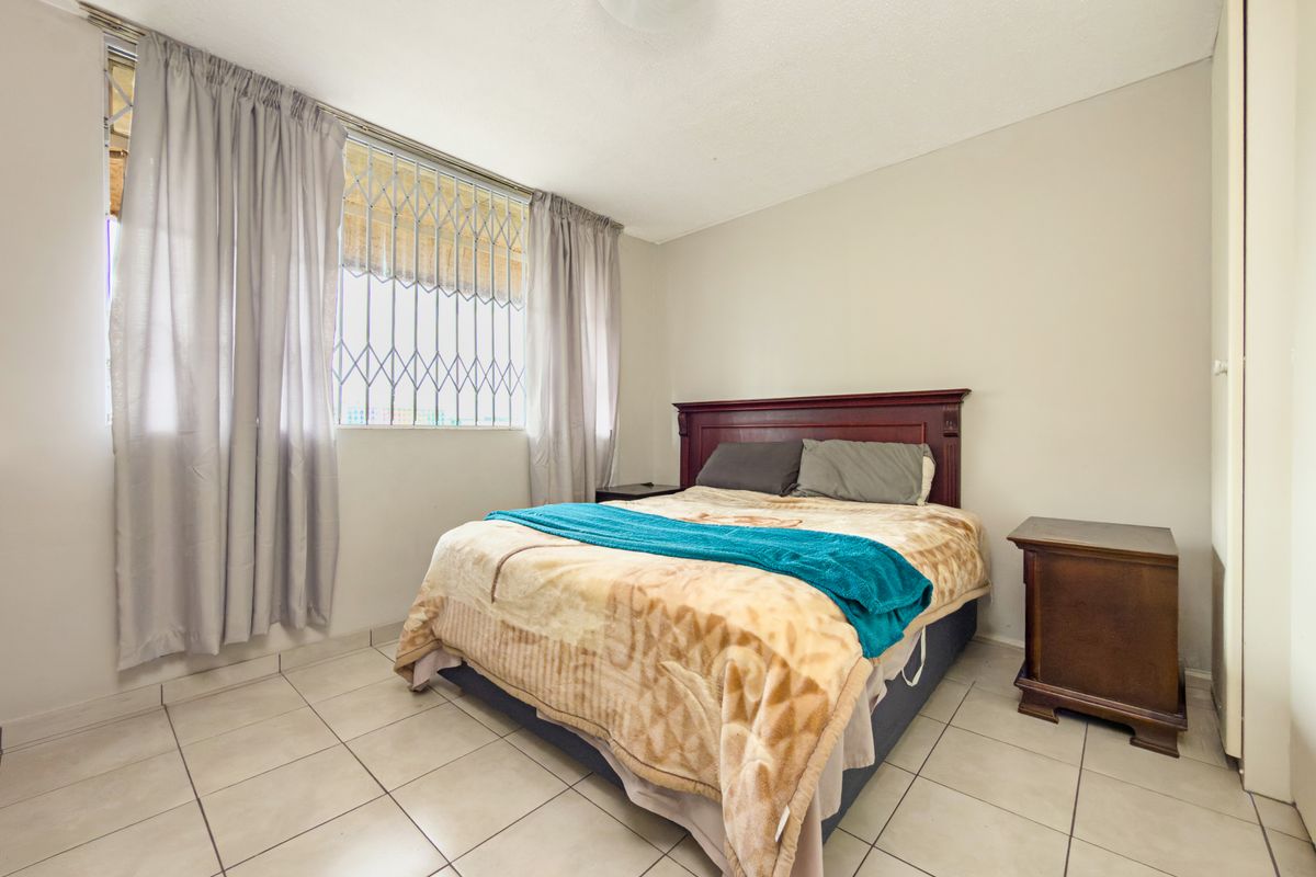 A functional bedroom featuring tiled flooring, security bars on the window, and a built-in cupboard for storage.