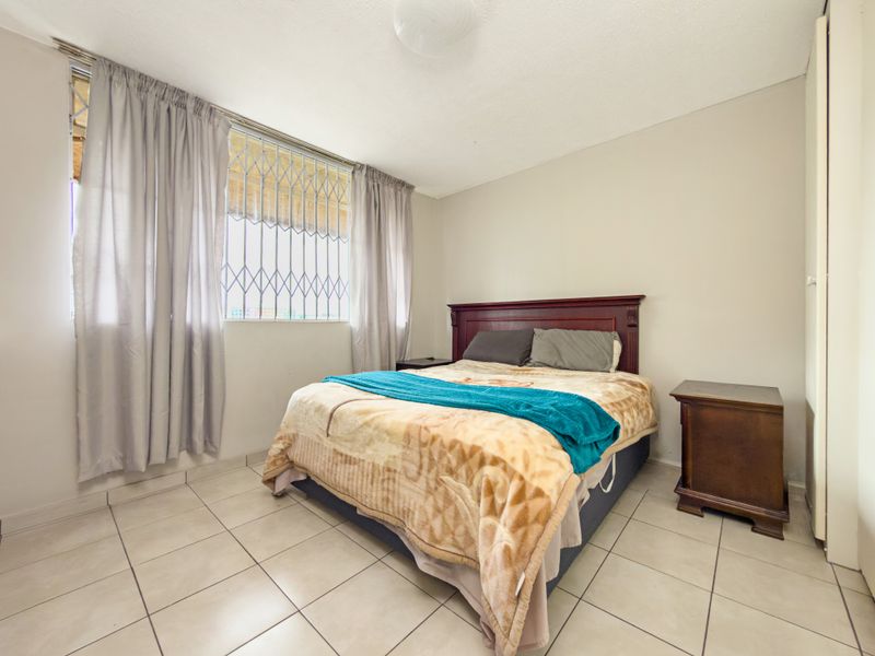 A functional bedroom featuring tiled flooring, security bars on the window, and a built-in cupboard for storage.