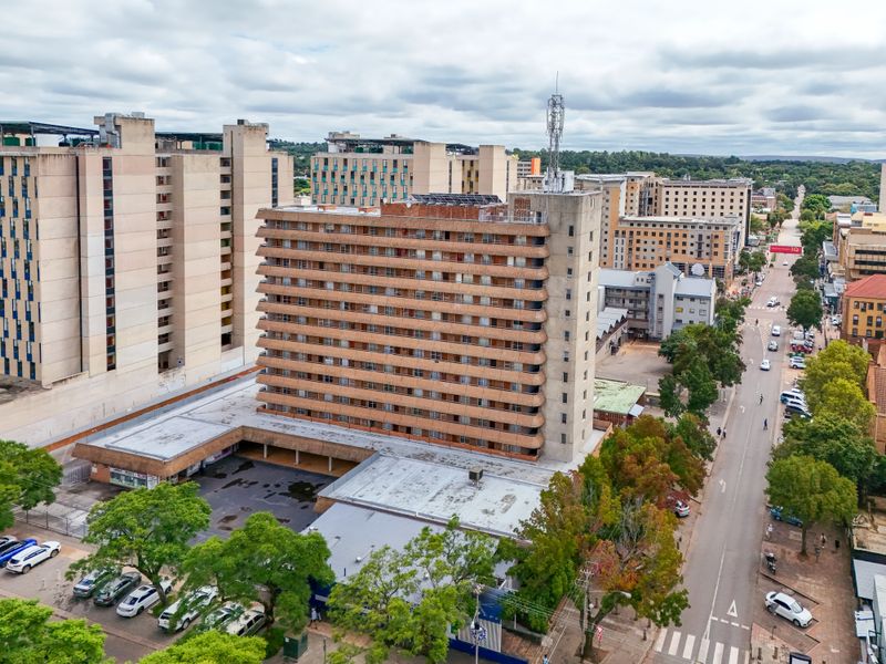 Aerial view of a multi-story apartment building featuring a concrete facade, private balconies, and rooftop solar infrastructure in an urban setting.
