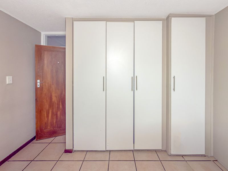 A bedroom featuring built-in white cupboards, tiled flooring, and a solid wood door, presenting a clean and functional space ready for personalization.