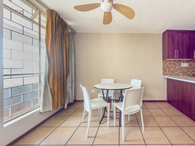 Open plan living and dining area featuring tiled floors, a ceiling fan, and a compact kitchen with built-in cabinetry and mosaic backsplash.