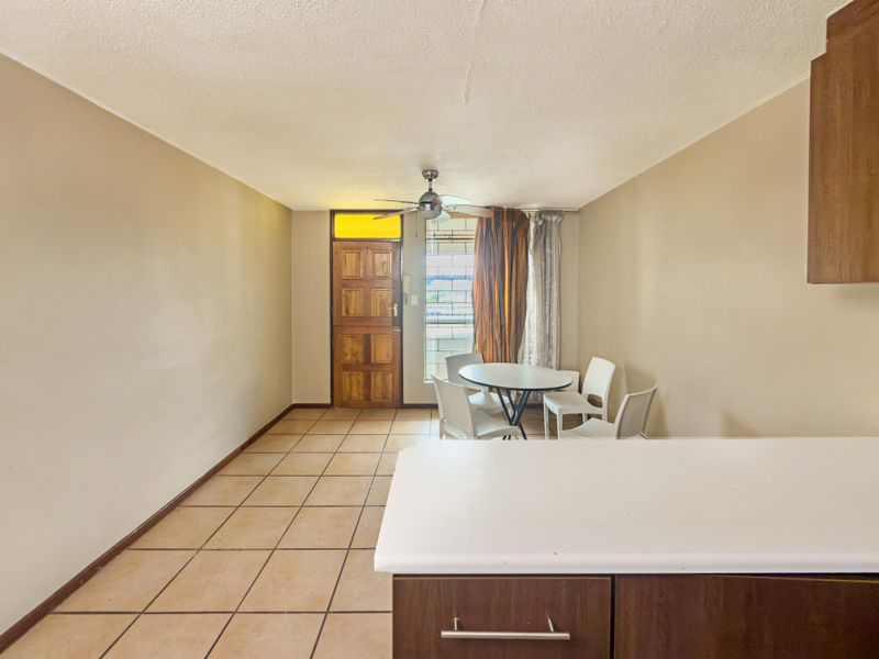 Open plan living and kitchen area featuring tiled flooring, a ceiling fan, and a solid wood entrance door with a transom window.