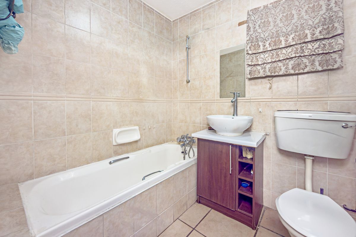 A functional bathroom featuring a bathtub, vanity with vessel sink, and toilet, finished with neutral ceramic wall and floor tiles.
