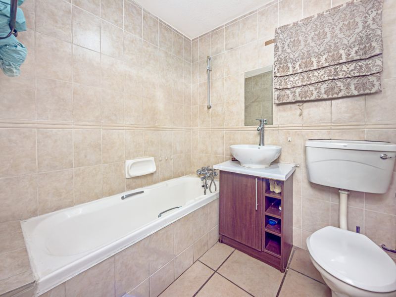 A functional bathroom featuring a bathtub, vanity with vessel sink, and toilet, finished with neutral ceramic wall and floor tiles.