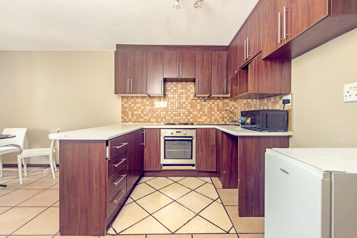 A functional kitchen featuring dark wood cabinetry, mosaic tile backsplash, built-in oven, and ceramic tiled flooring with a breakfast bar area.