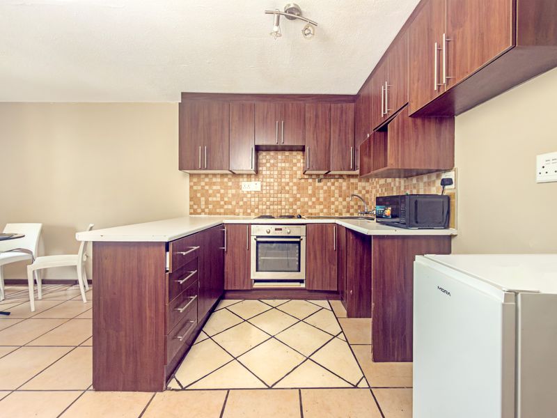 A functional kitchen featuring dark wood cabinetry, mosaic tile backsplash, built-in oven, and ceramic tiled flooring with a breakfast bar area.