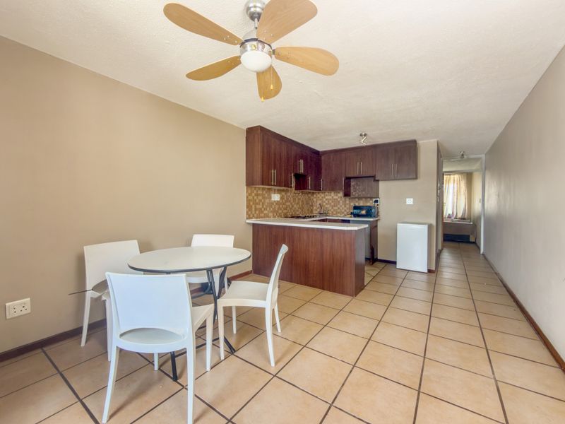 Open-plan living and kitchen area featuring tiled flooring, a ceiling fan, and wooden cabinetry with a mosaic tile backsplash.