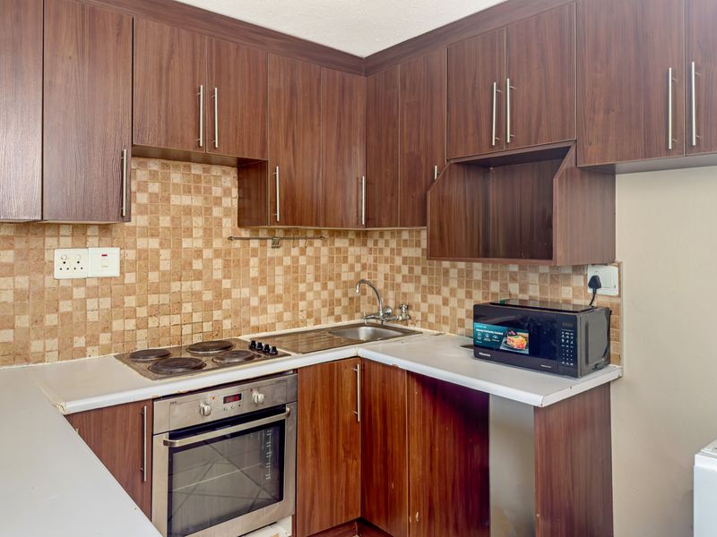 Compact kitchen featuring dark wood-look cabinetry, mosaic tile backsplash, integrated electric oven and hob, and a stainless steel sink.