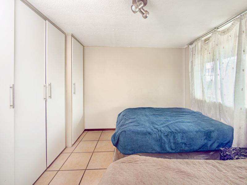 A bedroom featuring built-in cupboards, tiled flooring, and a ceiling spotlight fixture, offering a functional space with neutral wall finishes.