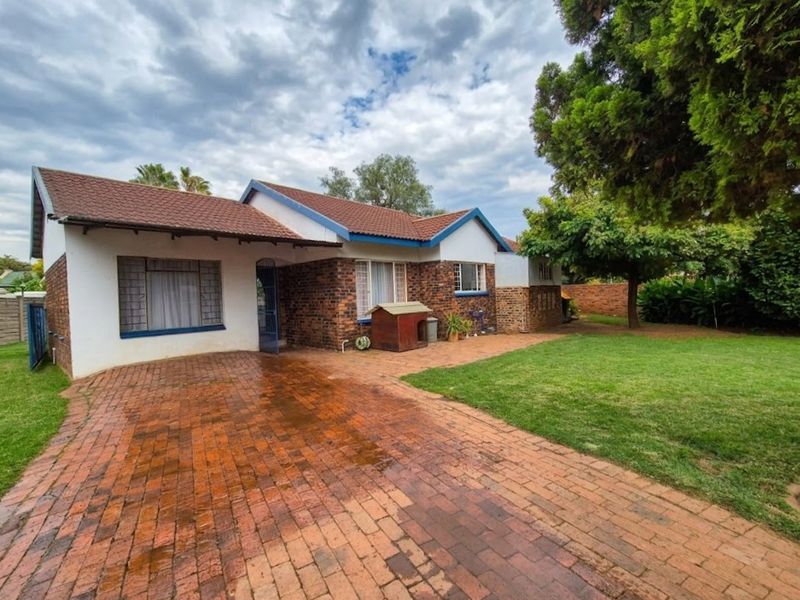 Rear view of a single-story brick house featuring a paved driveway, tiled roof, and a spacious garden area.