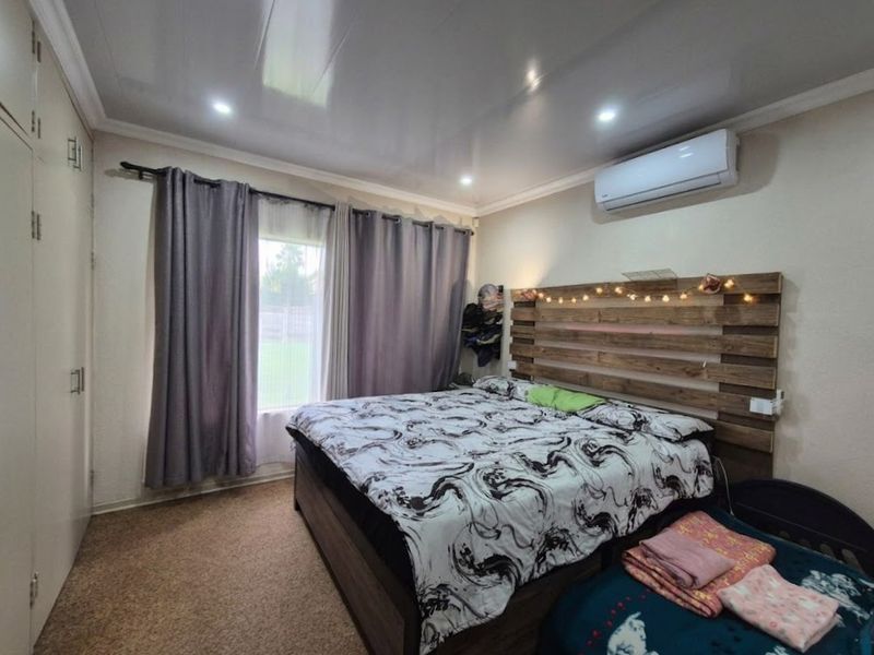 A bedroom featuring built-in cupboards, an air conditioning unit, and recessed downlights, providing a functional and comfortable living space.
