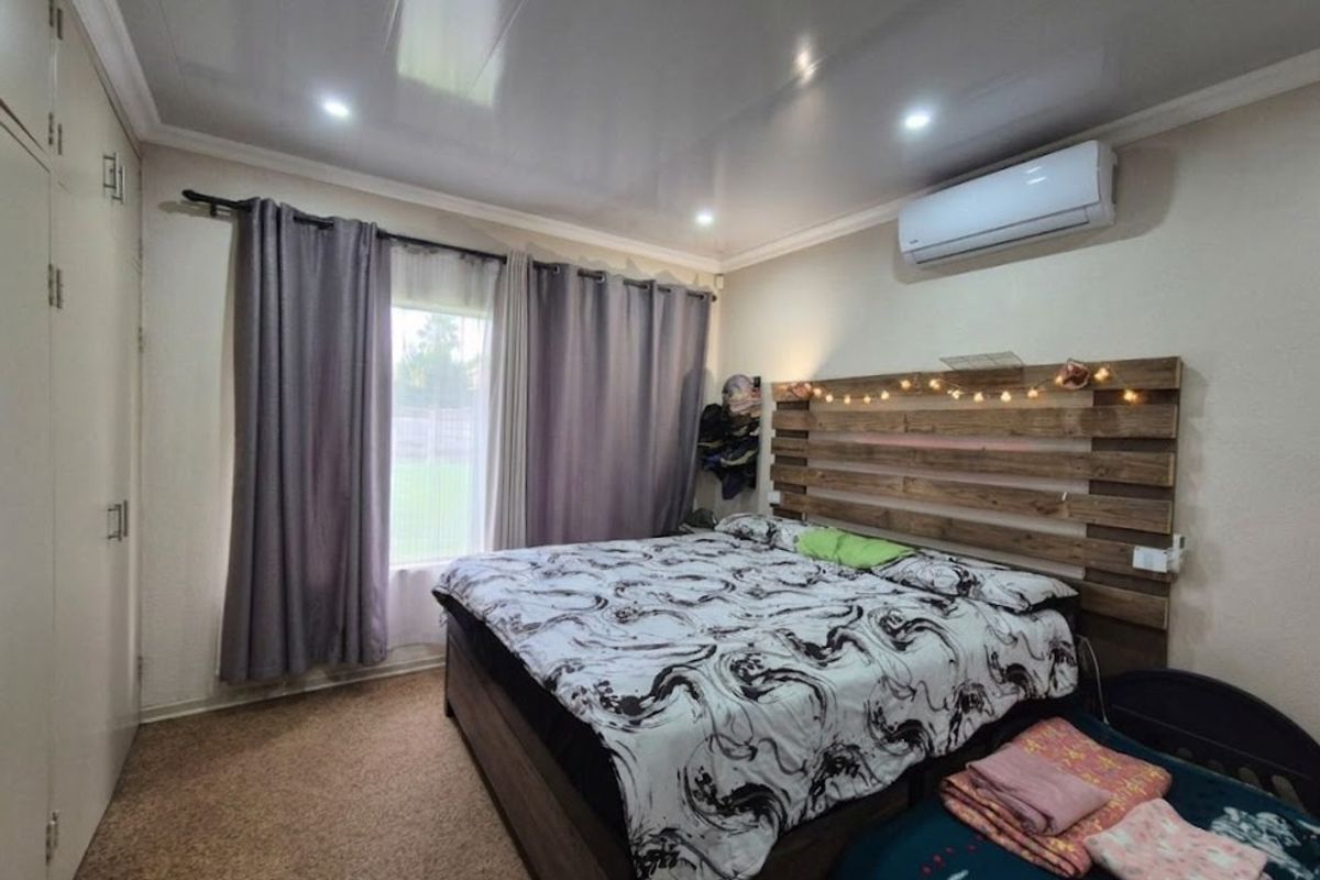 A bedroom featuring built-in cupboards, an air conditioning unit, and recessed downlights, providing a functional and comfortable living space.