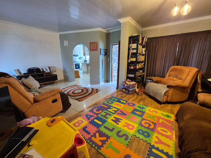 Spacious living area featuring a mix of tiled and laminate flooring, an arched entryway leading to the kitchen, and classic ceiling cornicing.