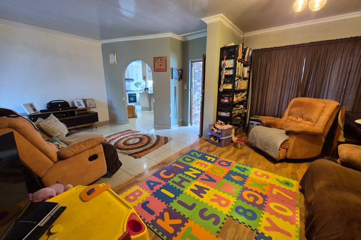 Spacious living area featuring a mix of tiled and laminate flooring, an arched entryway leading to the kitchen, and classic ceiling cornicing.