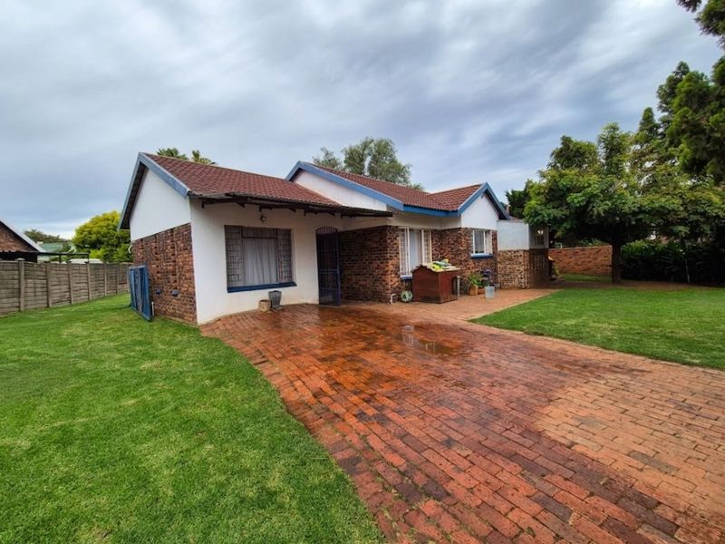 Front view of a single-story brick house featuring a tiled roof, paved driveway, and established garden area.