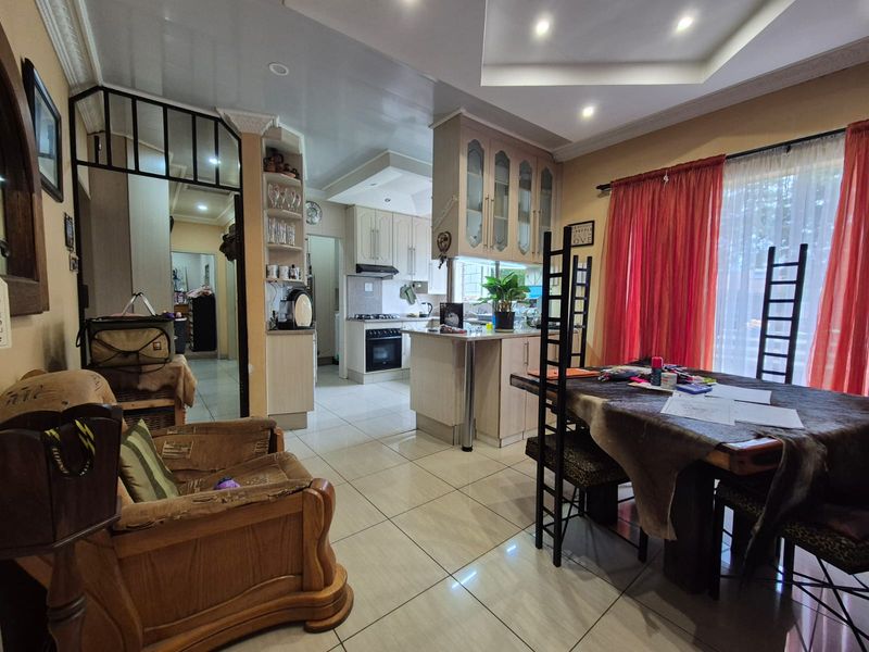 Open-plan living and dining area featuring a functional kitchen with built-in cabinetry, oven, and hob, complemented by tiled flooring and recessed ceiling lighting.