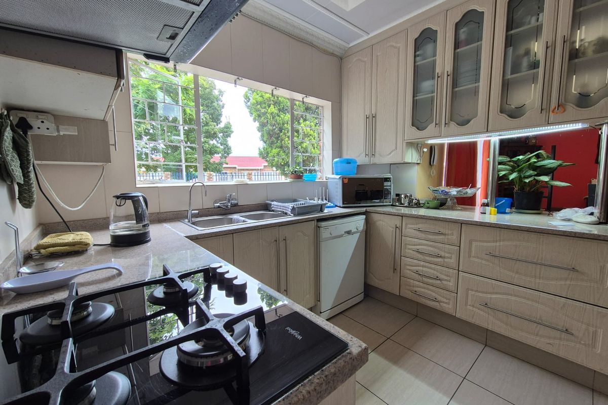 Functional kitchen featuring light wood-finish cabinetry, a gas hob with extractor fan, double sink, and tiled flooring with ample natural light.