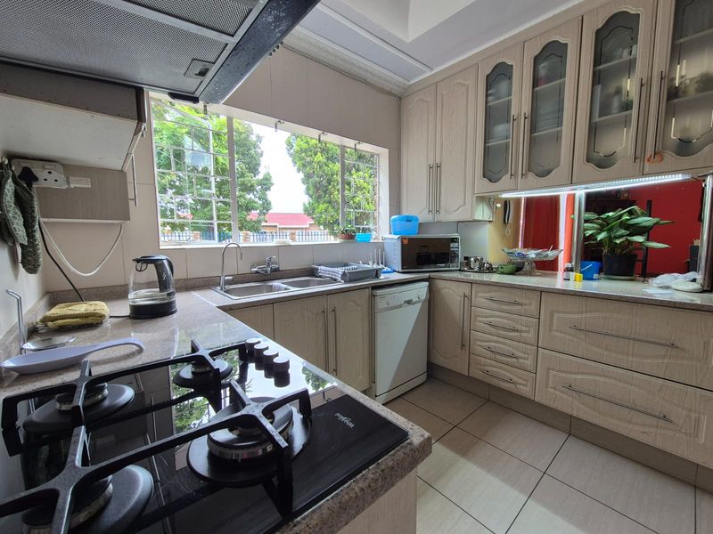 Functional kitchen featuring light wood-finish cabinetry, a gas hob with extractor fan, double sink, and tiled flooring with ample natural light.