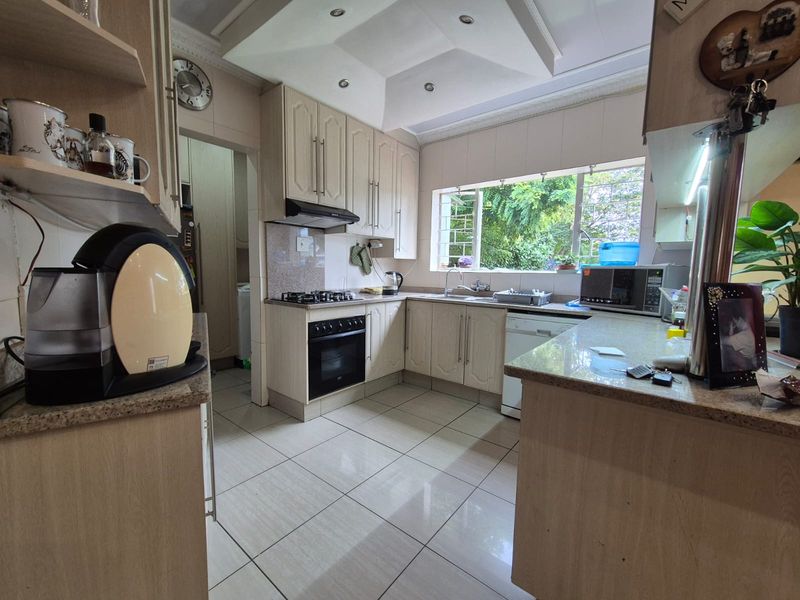 A functional kitchen featuring light-toned cabinetry, granite countertops, a gas hob with an integrated oven, and tiled flooring with ample natural light.