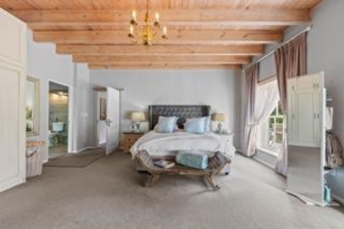 Spacious bedroom featuring exposed timber beam ceilings, neutral carpeting, and an en-suite bathroom access.