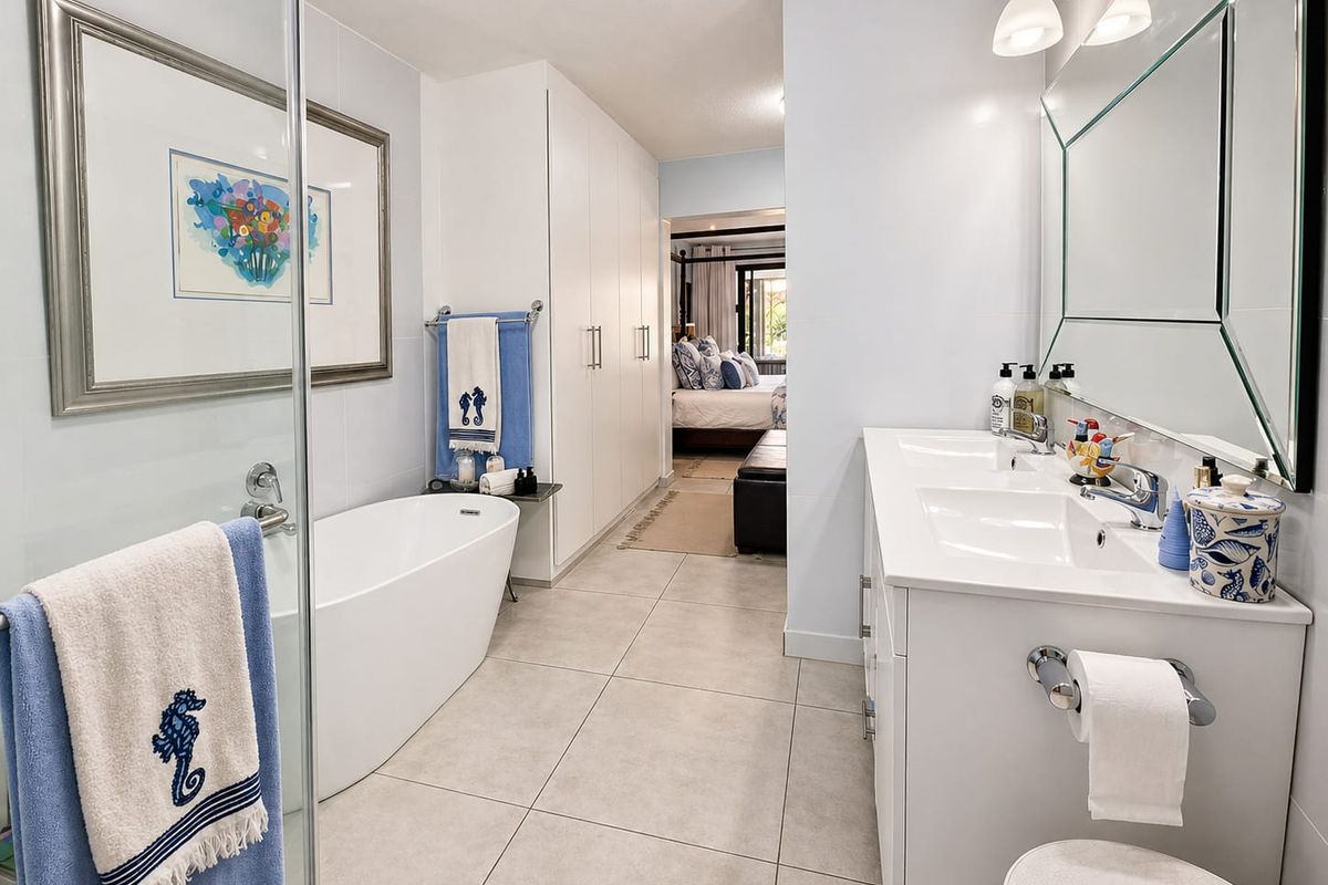Modern bathroom featuring a double vanity, freestanding bathtub, glass-enclosed shower, and ample built-in storage cabinetry with neutral floor tiling.