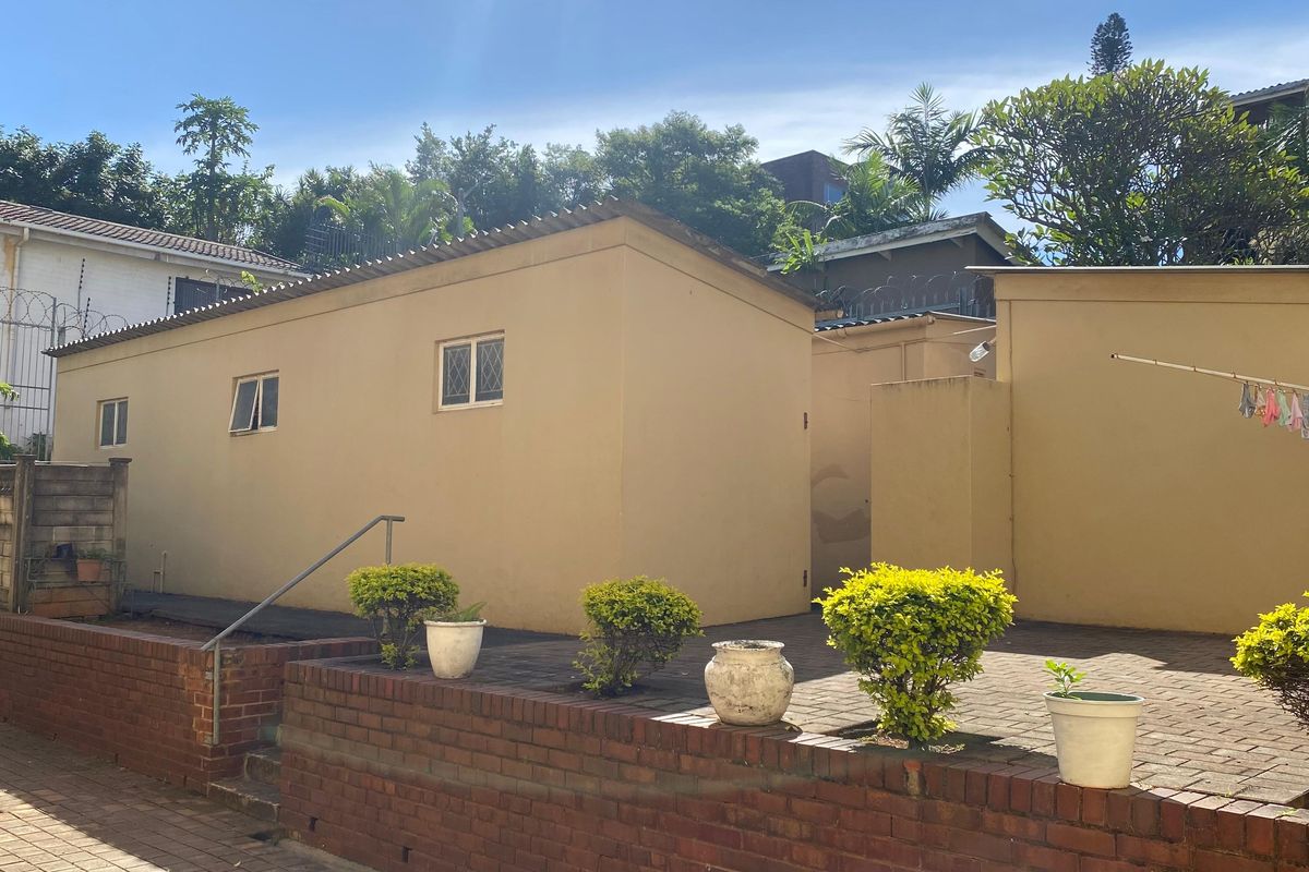 Rear exterior view of the property featuring a paved courtyard, brick retaining wall, and security fencing.