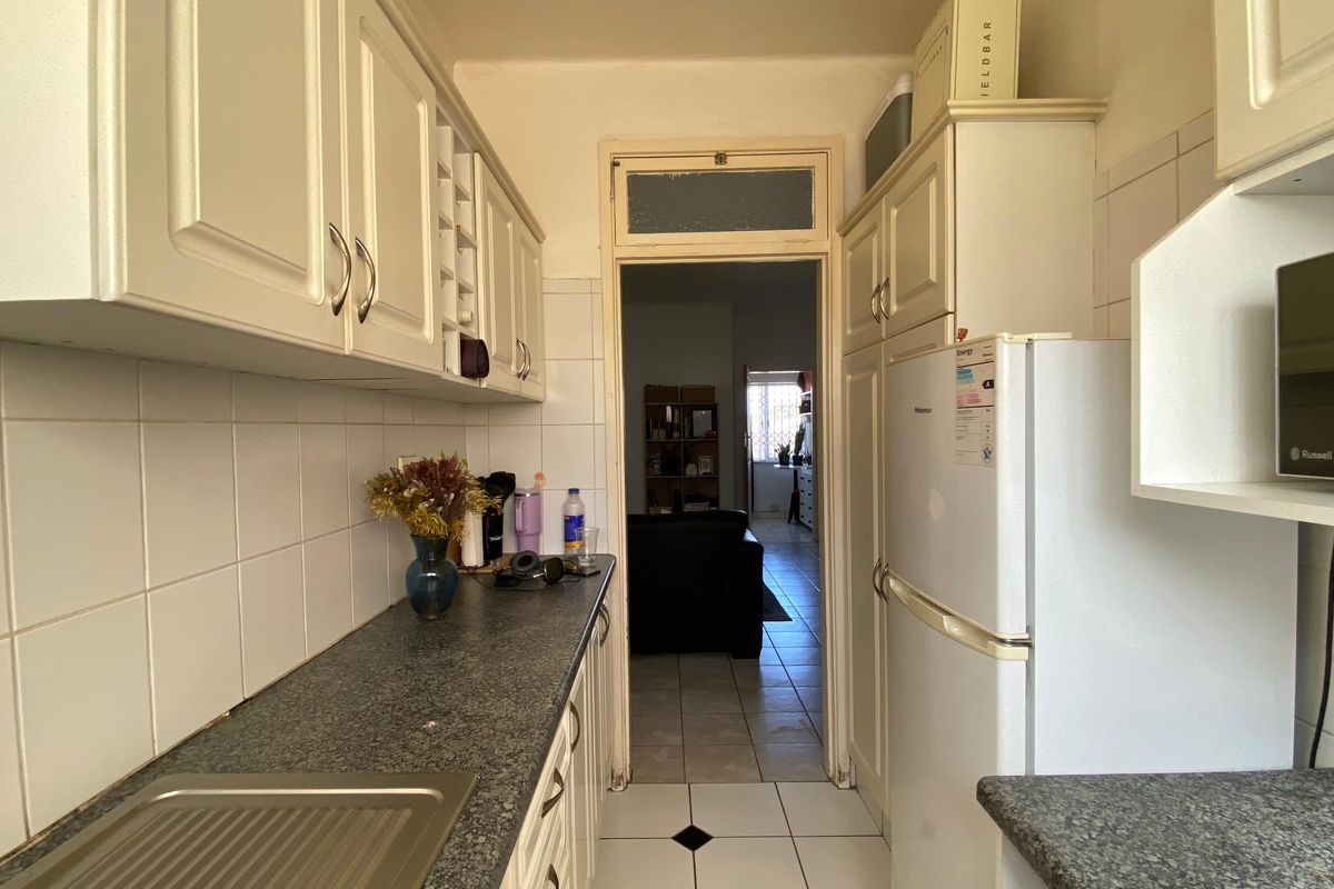 A functional galley-style kitchen featuring white built-in cabinetry, dark laminate countertops, and tiled finishes, offering a practical layout with direct access to the living area.