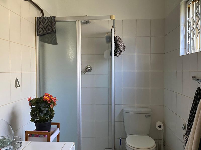 A functional bathroom featuring a shower enclosure, toilet, and tiled walls, equipped with a security gate on the window for added peace of mind.