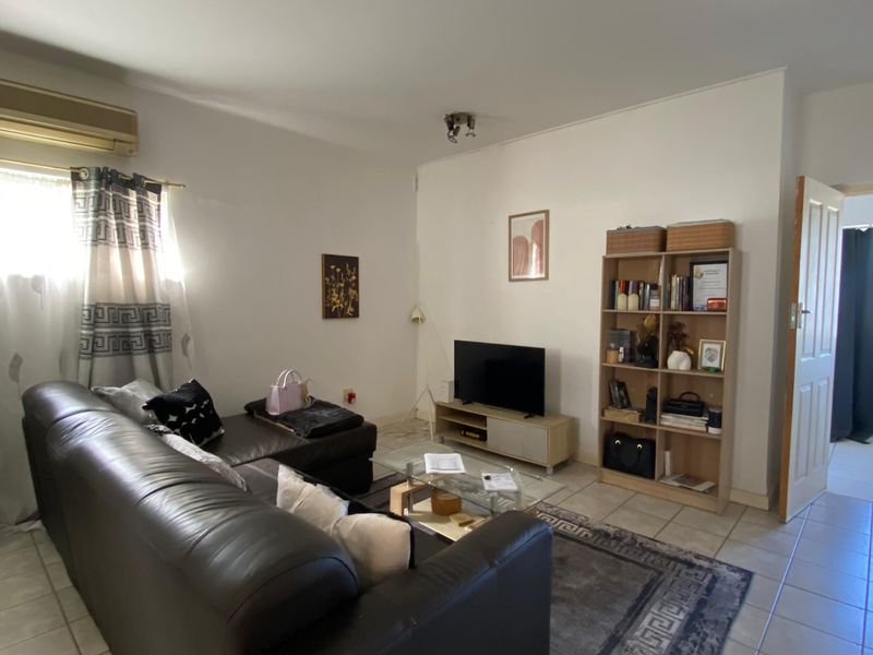 A living room featuring tiled flooring and a wall-mounted air conditioning unit, with an open doorway leading to an adjacent space.