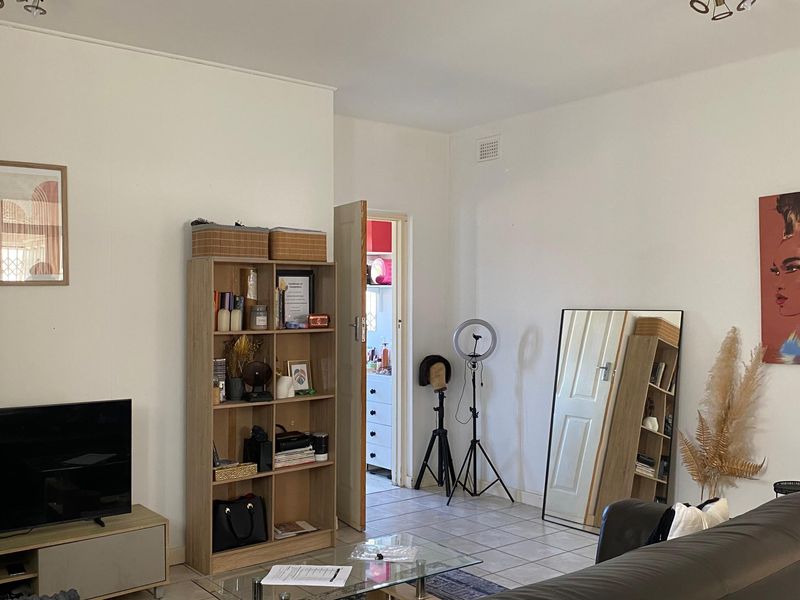 A living room featuring tiled flooring and neutral wall finishes, providing a functional space with access to an adjacent room.
